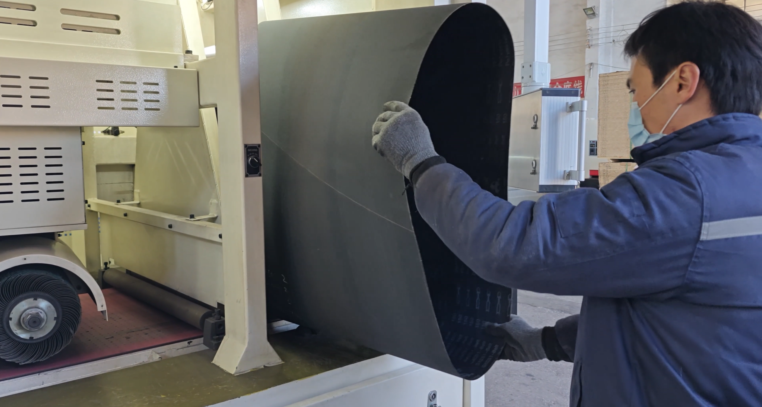 Worker replacing sanding belt on industrial sanding machine in factory workshop