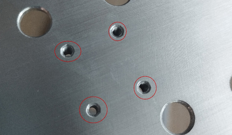 Close-up inspection of residual burrs and edge defects around drilled holes on a ground metal plate